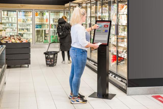 A supermarket customer interacting with a freestanding SpacePole Self-Service Kiosk™.